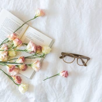 white and pink flowerson a book beside eyeglasses