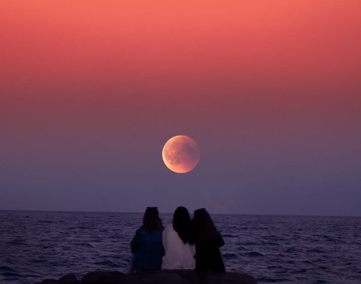 women sitting on rock infront of ocean