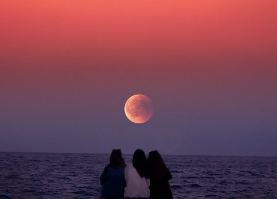 women sitting on rock infront of ocean