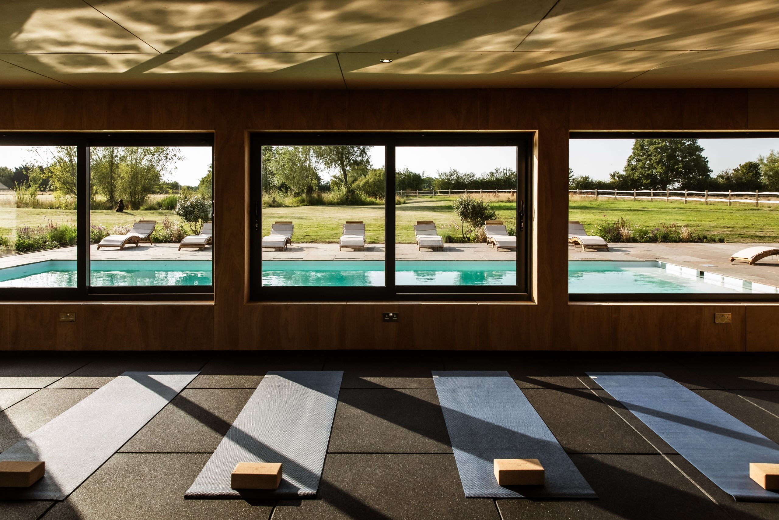 yoga mats in studio facing a blue outdoor swimming pool and green garden