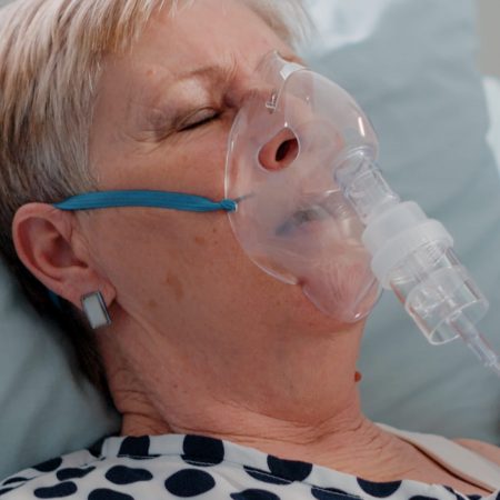 Doctor and nurse giving assistance to heavy breathing woman, using oxygen tube to cure respiratory issues in bed. Medical team helping aged patient with hyperventilating illness.