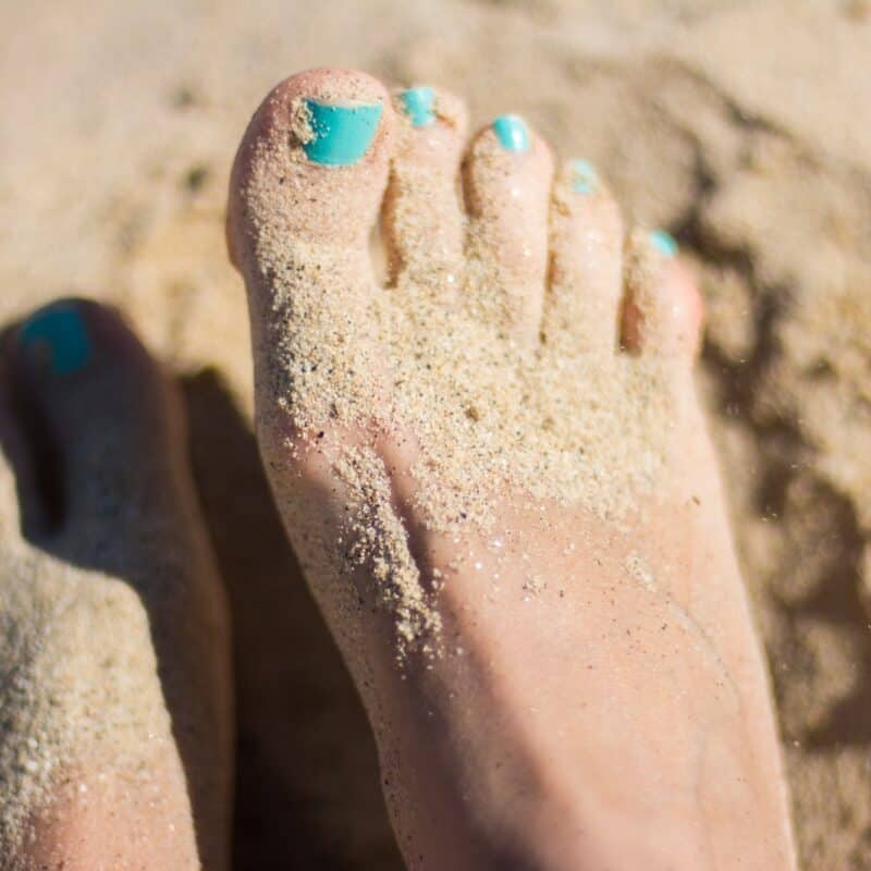 person sky-blue nail polish feet on brown sand