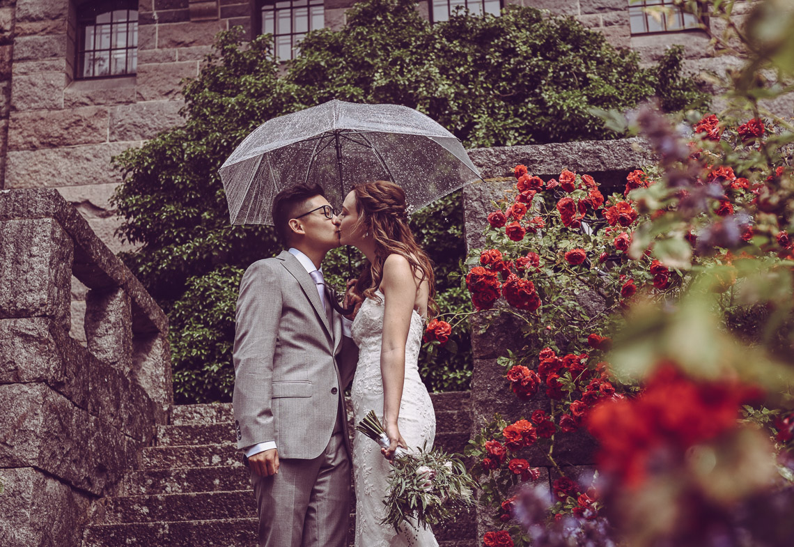 bröllopsporträtt vid Teleborgs slott rosenbuskar brudpar i regn med paraply