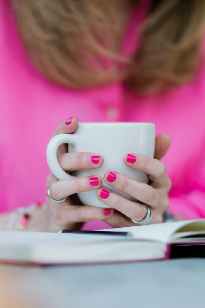 Closeup on Womans Hands with Pink Nails Holding White Ceramic Mug