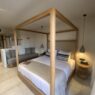 Elegant bedroom at Stella Blue Crete featuring a wooden four-poster bed, neutral earthy decor and a bright balcony overlooking palm trees.