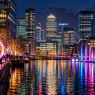 Editorial illustration of Canary Wharf illuminated with colourful light installations at night.