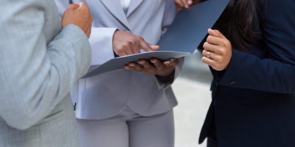 Cropped shot of business people with folder. Mid section of business colleagues standing together and looking at papers in folder. Teamwork concept