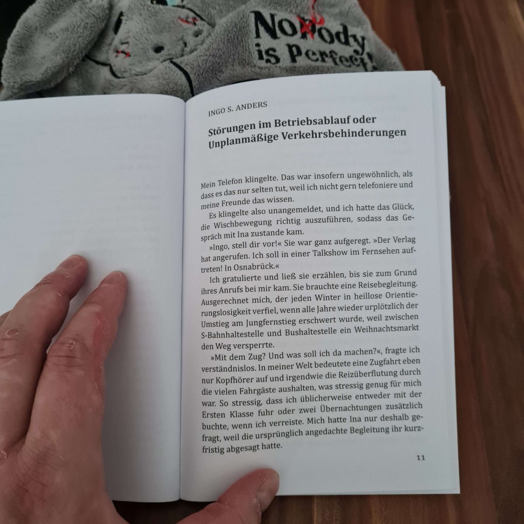 Eine aufgeschlagene Buchseite. Schwarze Schrift auf weißem Grund: Ingo S. Anders Störungen im Betriebsablauf oder Unplanmäßige Verkehrsbehinderungen Mein Telefon klingelte. Das war insofern ungewöhnlich, als dass es das nur selten tut, weil ich nicht gern telefoniere und meine Freunde das wissen. Es klingelte also unangemeldet, und ich hatte das Glück, die Wischbewegung richtig auszuführen, sodass das Gespräch mit Ina zustande kam. "Ingo, stell dir vor!" Sie war ganz aufgeregt. "Der Verlag hat angerufen. Ich soll in einer Talkshow im Fernsehen auftreten! In Osnabrück." Ich gratulierte und ließ sie erzählen, bis sie zum Grund ihres anrufs bei mir kam. Sie brauchte eine Reisebegleitung. Ausgerechnet mich, der jeden Winter in heillose Orientierungslosigkeit verfiel, wenn alle Jahre wieder urplötzlich der Umstieg am Jungefernstieg erschwert wurde, weil zwischen S-Bahnhaltestelle und Bushaltestelle ein Weihnachtsmarkt den Weg versperrte. "Mit dem Zug? Und was soll ich da machen?", fragte ich verständnislos. In meiner Welt bedeutete eine Zugfahrt eben nur Kopfhörer auf und irgendwie die Reizüberflutung durch die vielen Fahrgäste aushalten, was stressig genug für mich war. So stressig, dass ich üblicherweise entweder mit der Ersten Klasse fuhr oder zwei Übernachtungen zusätzlich buchte, wenn ich verreiste. Mich hatte Ina nur deshalb gefragt, weil die ursprünglich angedachte Begleitung ihr kurzfristig abgesagt hatte.