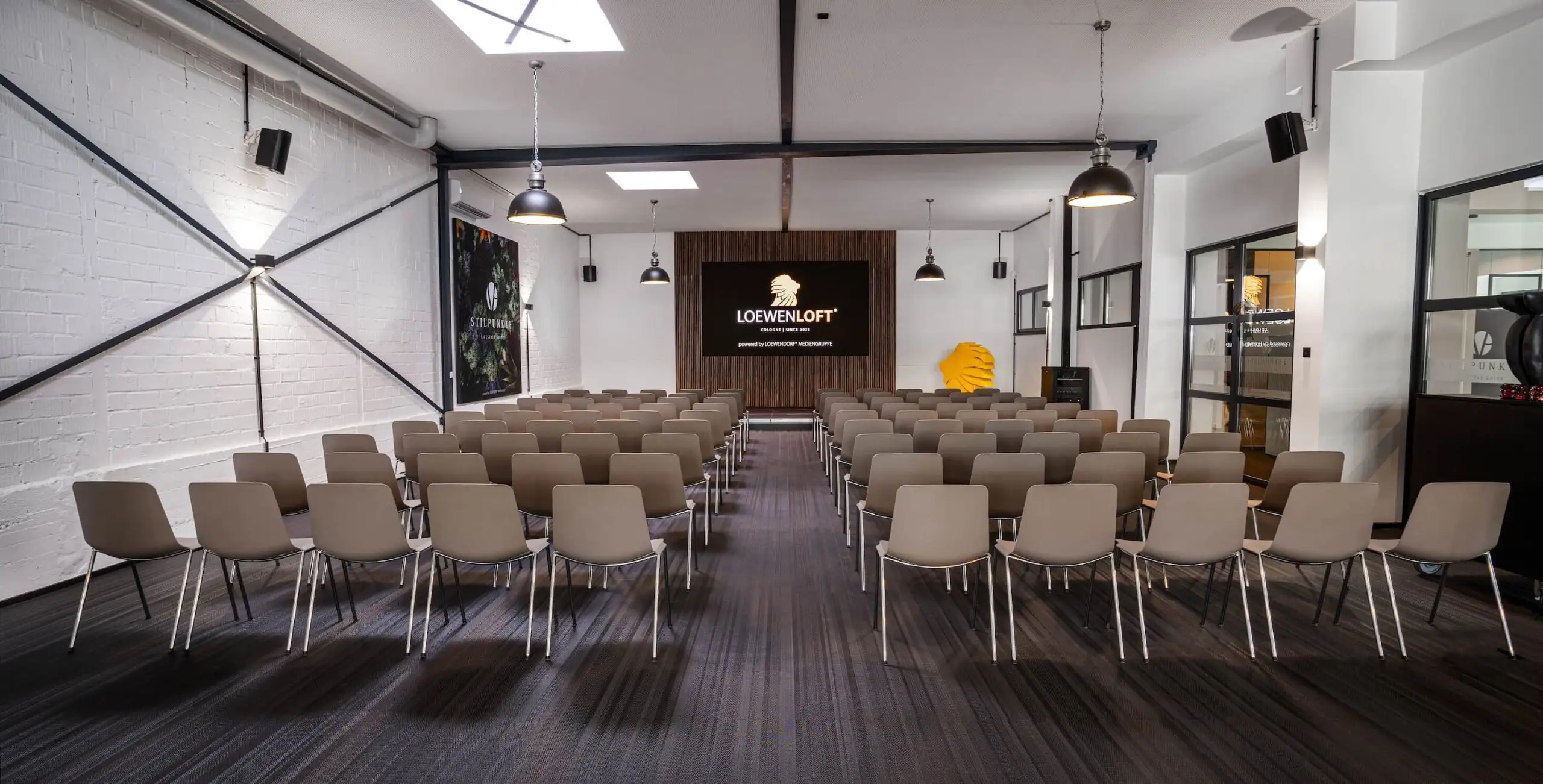 Eventsaal mit Bühne, Stuhlreihen und moderner Architektur.