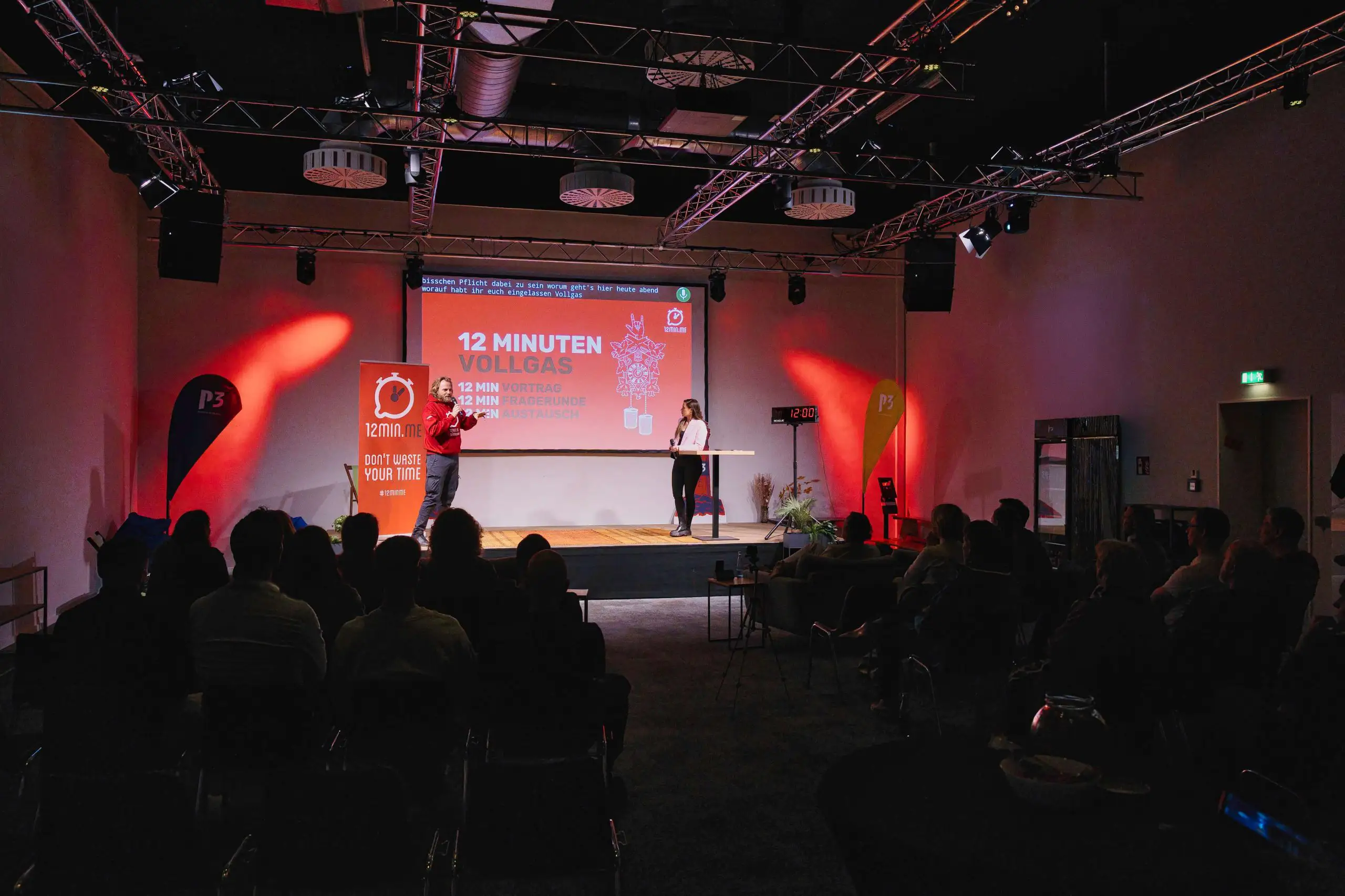 2 Personen stehen auf der Bühne und halten einen Vortrag vor Publikum