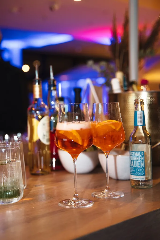 Zwei Aperol Spritz Gläser stehen auf einer Bar.