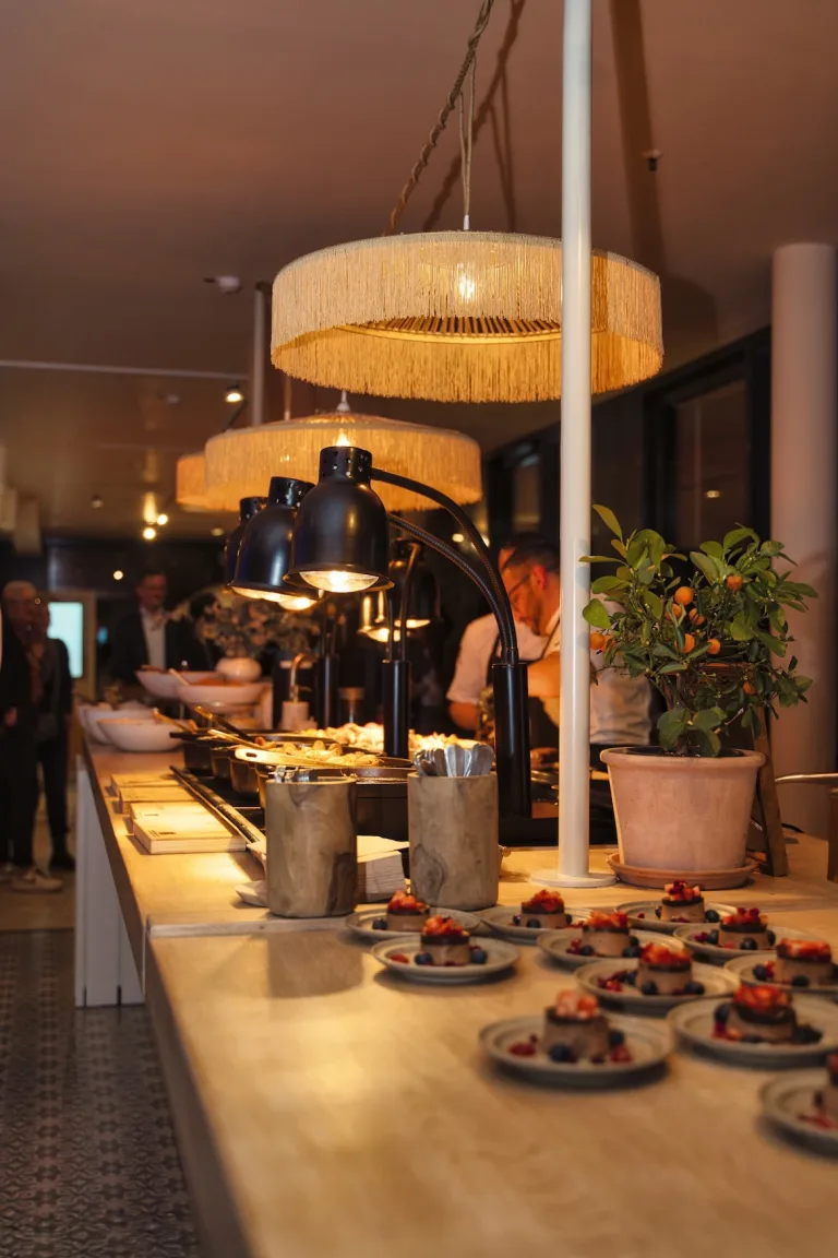 Stilvoll arrangiertes Catering-Buffet mit Wärmelampen und Fransen-Lampen in der Sturmfreien Bude Düsseldorf – Eventfotografie von Schwarzekreide Media, Eventfotografin Düsseldorf.
