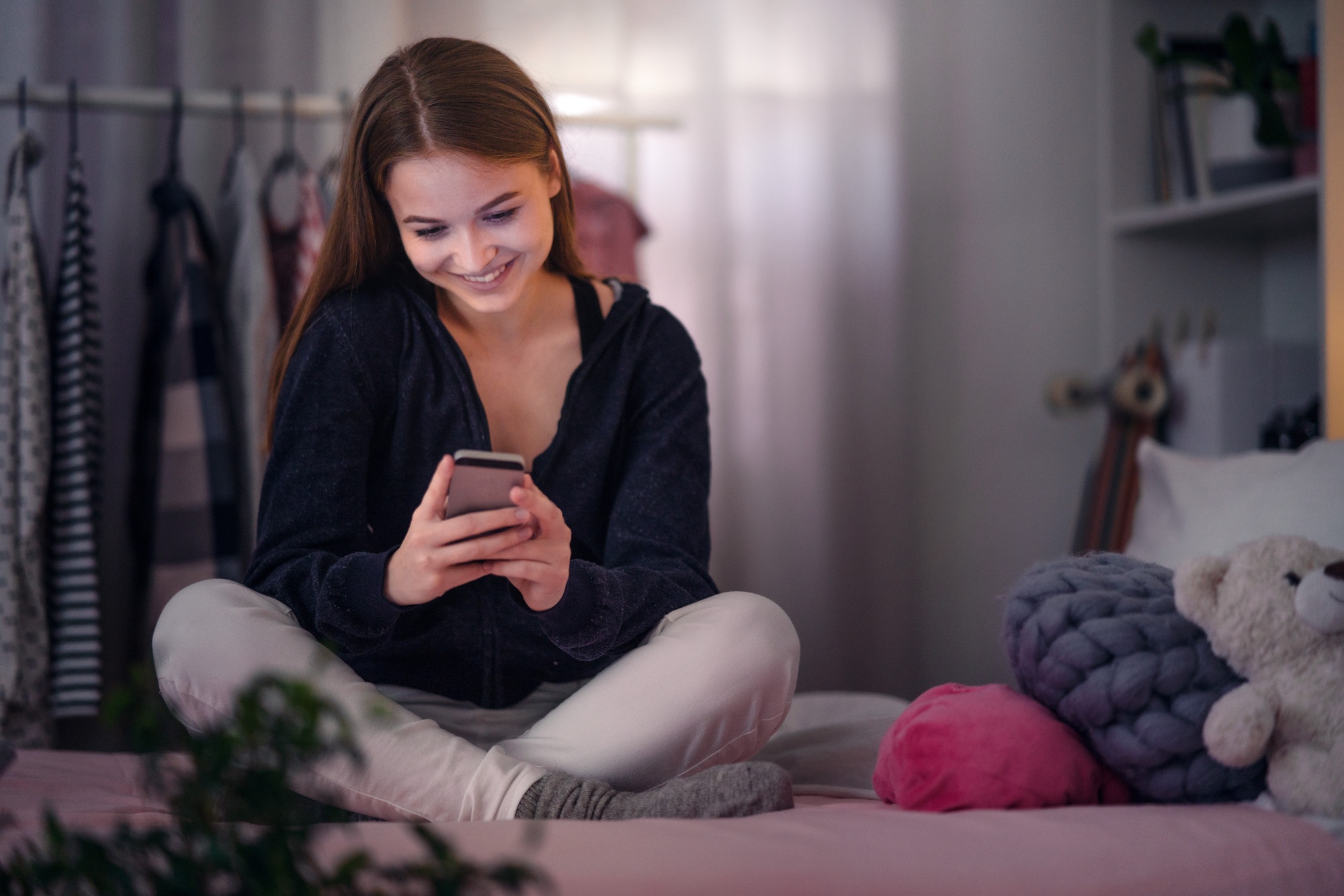 Happy young girl using smartphone on bed, online dating concept