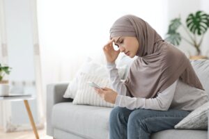 Upset Arab Girl In Hijab Looking At Smartphone Screen At Home
