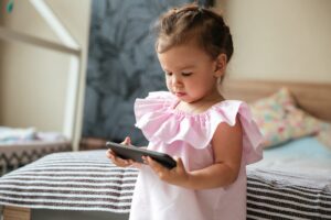 Serious little girl child indoors using mobile phone.