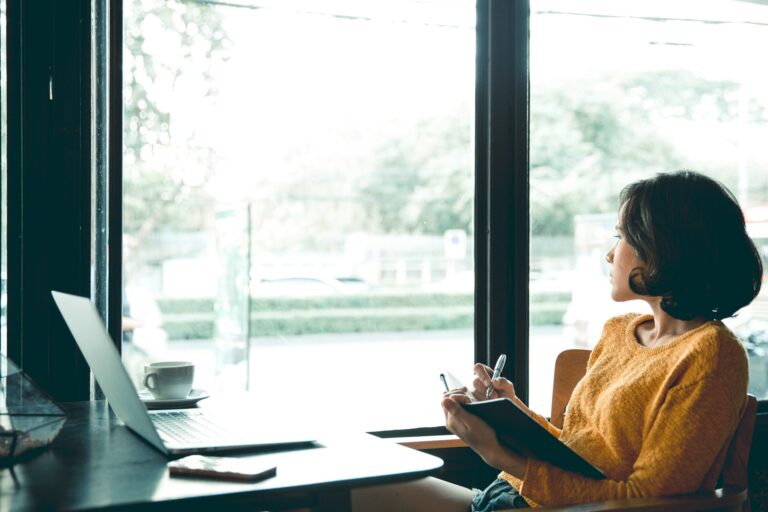 A woman in yellow sweater thinking about her freelance job. Working with laptop in the coffee shop.