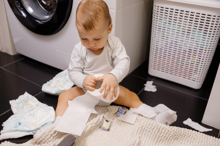 the child sits on a white toilet hands is toilet paper