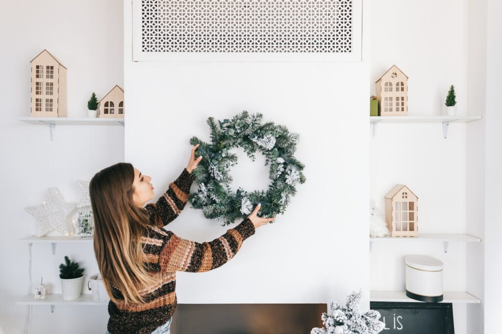 Young woman decorates the house for christmas, hangs a wreath on the wall.