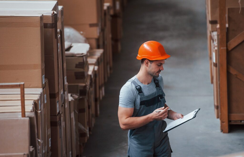 Storage worker in uniform and notepad in hands checks production