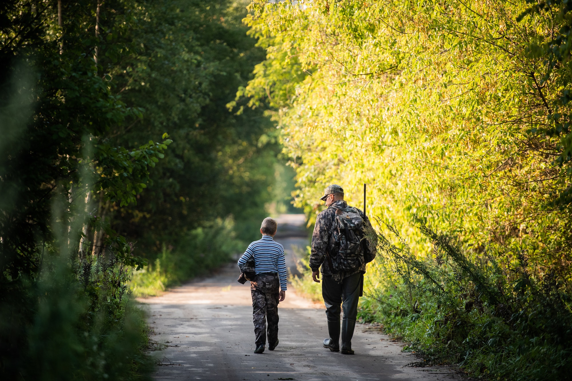 Hunters with hunting equipment going away through rural forest at sunrise during hunting season in