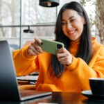 Smiling asian woman playing online game on cellphone in cafe