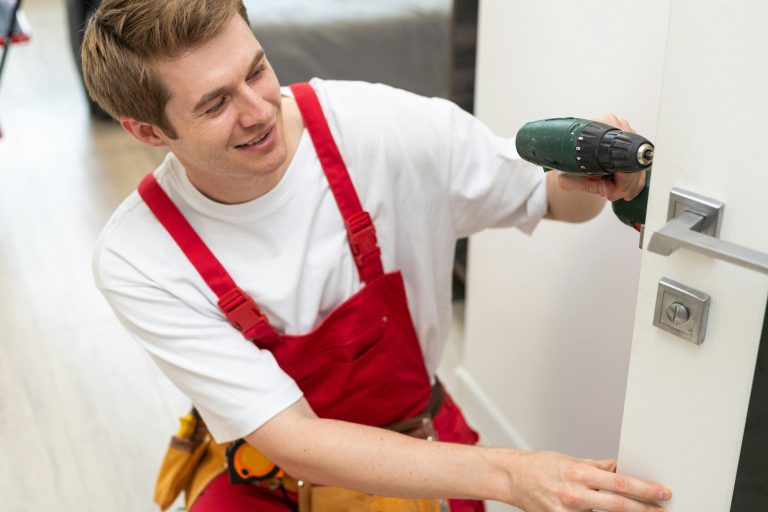 Installation of a lock on the front wooden entrance door. Portrait of young locksmith workman in