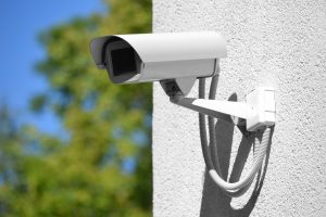 Telecamera di sicurezza esterna installata su un muro bianco, con cavi protetti e un'area verde sullo sfondo.