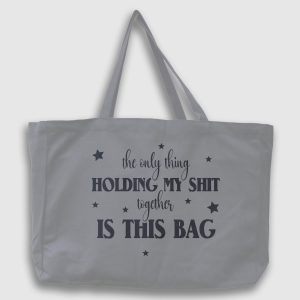 Foto på grå tygväska med svart text på engelska: "the only thing holding my shit together is this bag"
