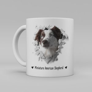 Vit keramikmugg med illustration av ett hundhuvud som "tittar ut genom" ett illustrerat hål. Hunden är av rasen miniatur american shepherd