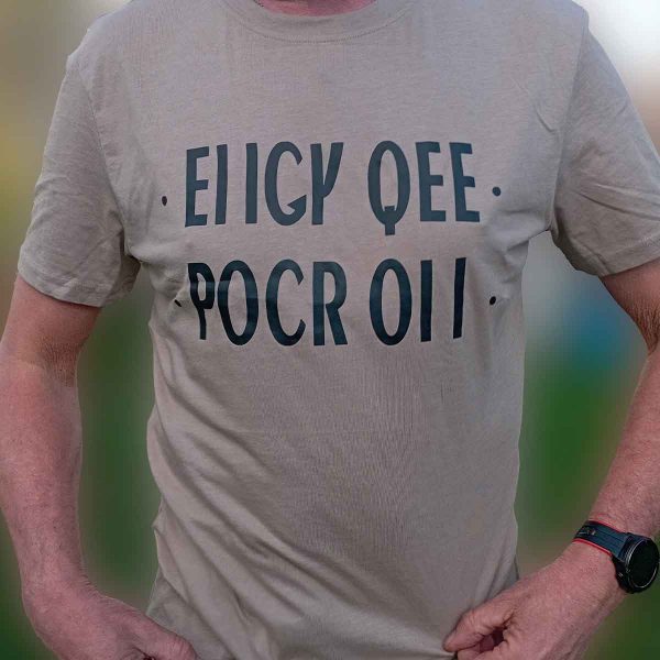 Foto på beige t-shirt med svart text: "EIIGY QEE POCR OII"