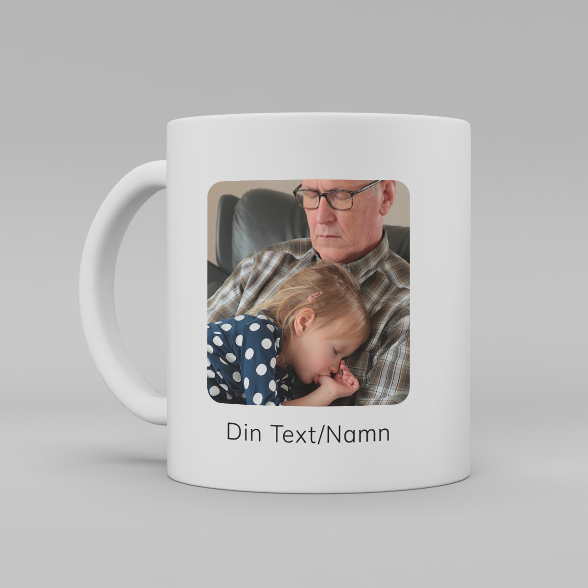 foto av en vit keramikmugg med ett foto av enman med ett barn i sin famn. Under "foto"står text "Egen text/namn" på muggen.
