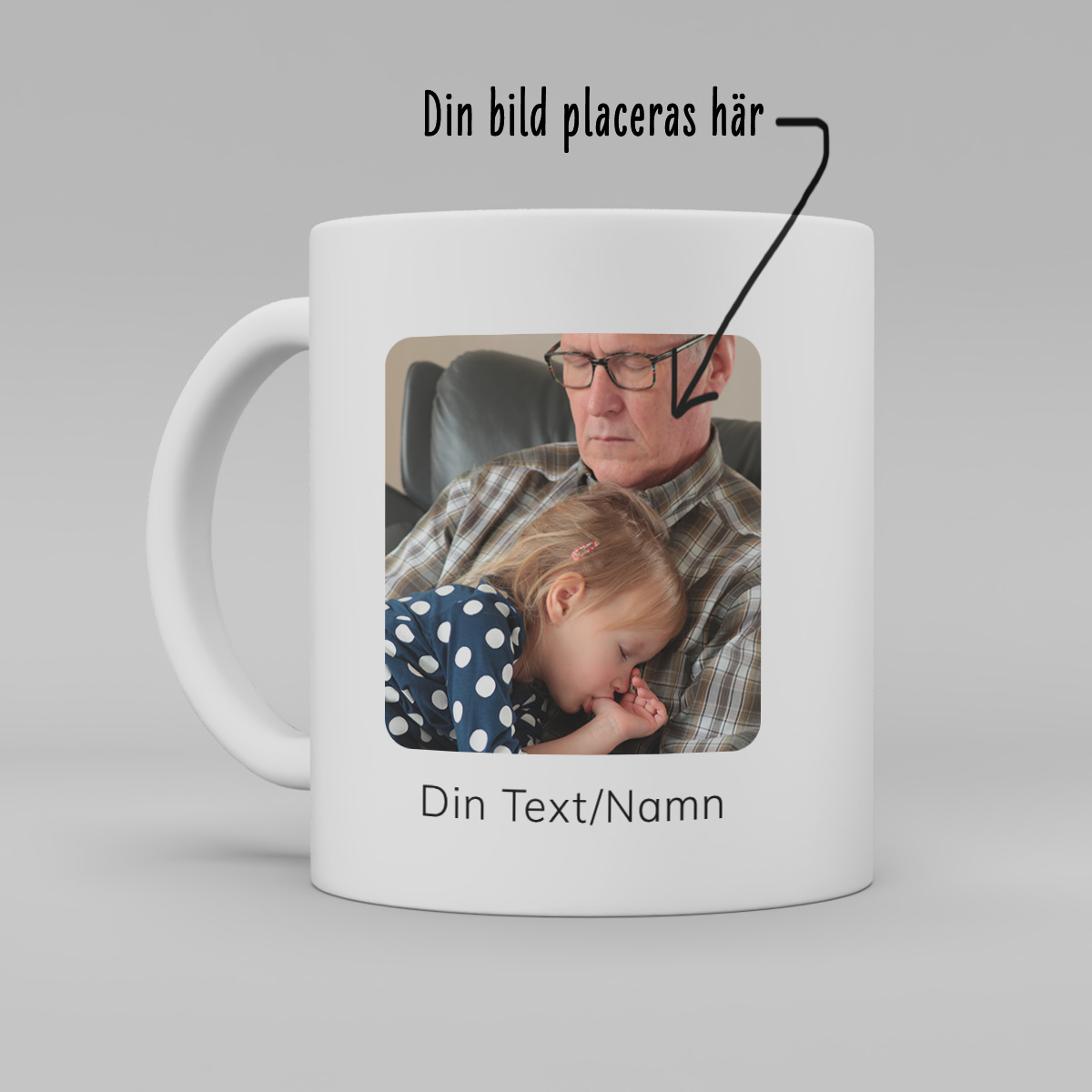 foto av en vit keramikmugg med ett foto av en man med ett barn i sin famn. Fotot är kvadratiskt. Under "foto"står text "Egen text/namn" på muggen. Ovanför "muggen" står texten: "Din bild placeras här" och en pil som pekar till fotot på muggen.