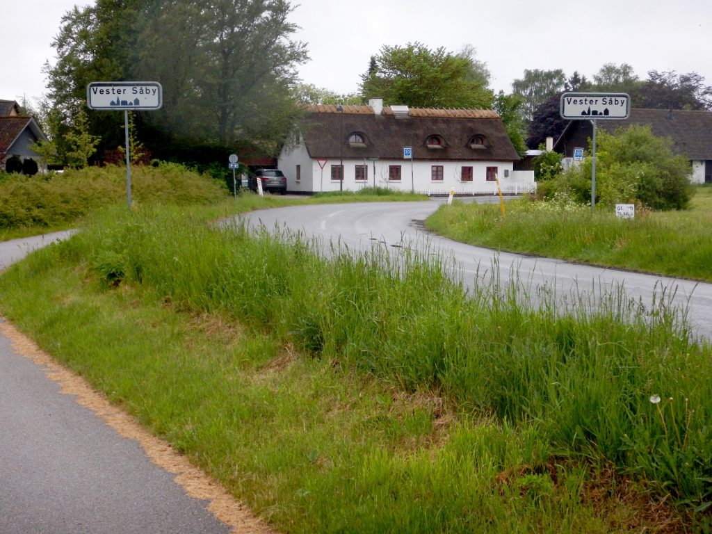 Vej der fører ind i Vester Såby med en hvid, stråtægt hus