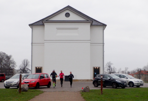 Bagsiden af kirken. Tre løbere og fire parkerede biler.