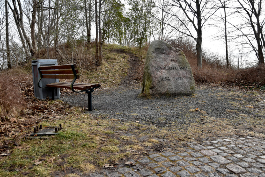 En bænk og en genforeningssten foran rundhøj.