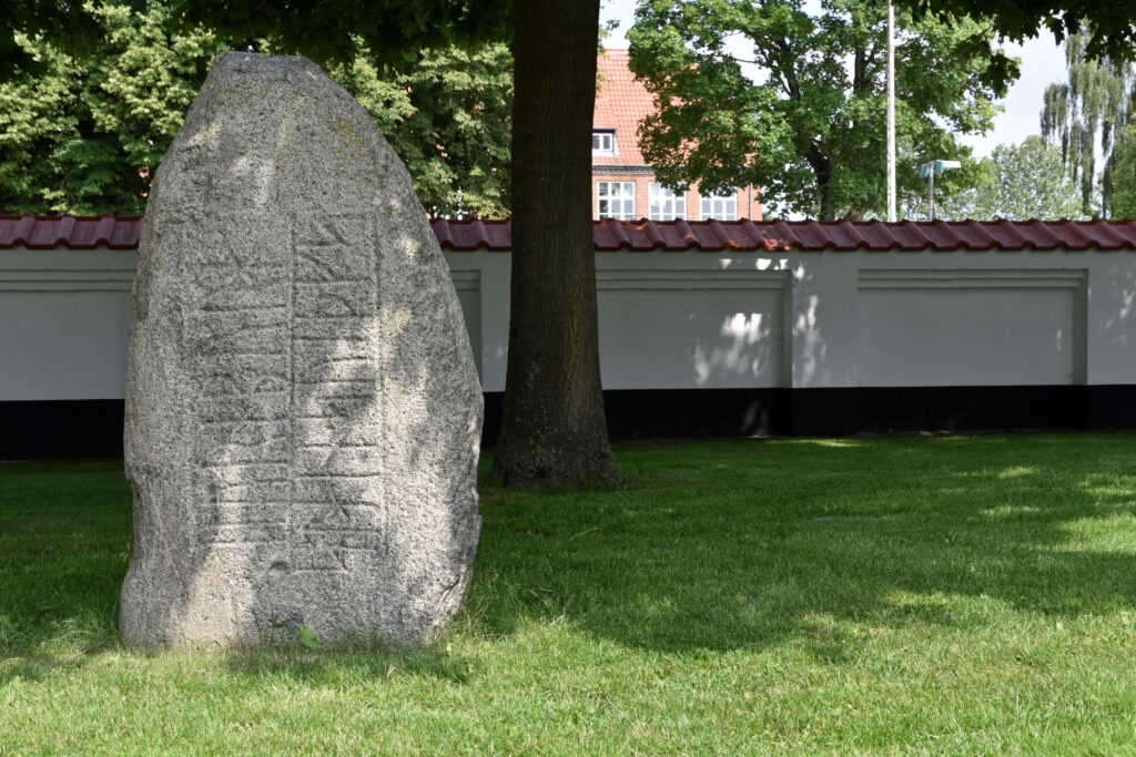 Runesten på grænplæne foran mur