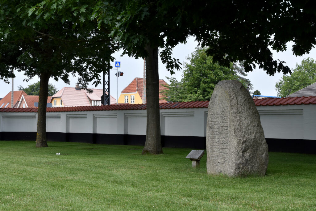 Runesten på grænplæne foran mur