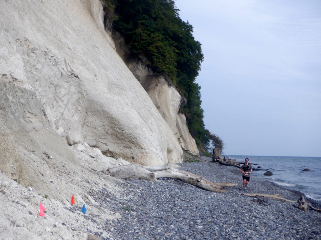 En stejl klint. En stenet strand og havet.