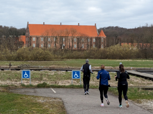 3 løbere. Et grønt område og en stor bygning af røde mursten.