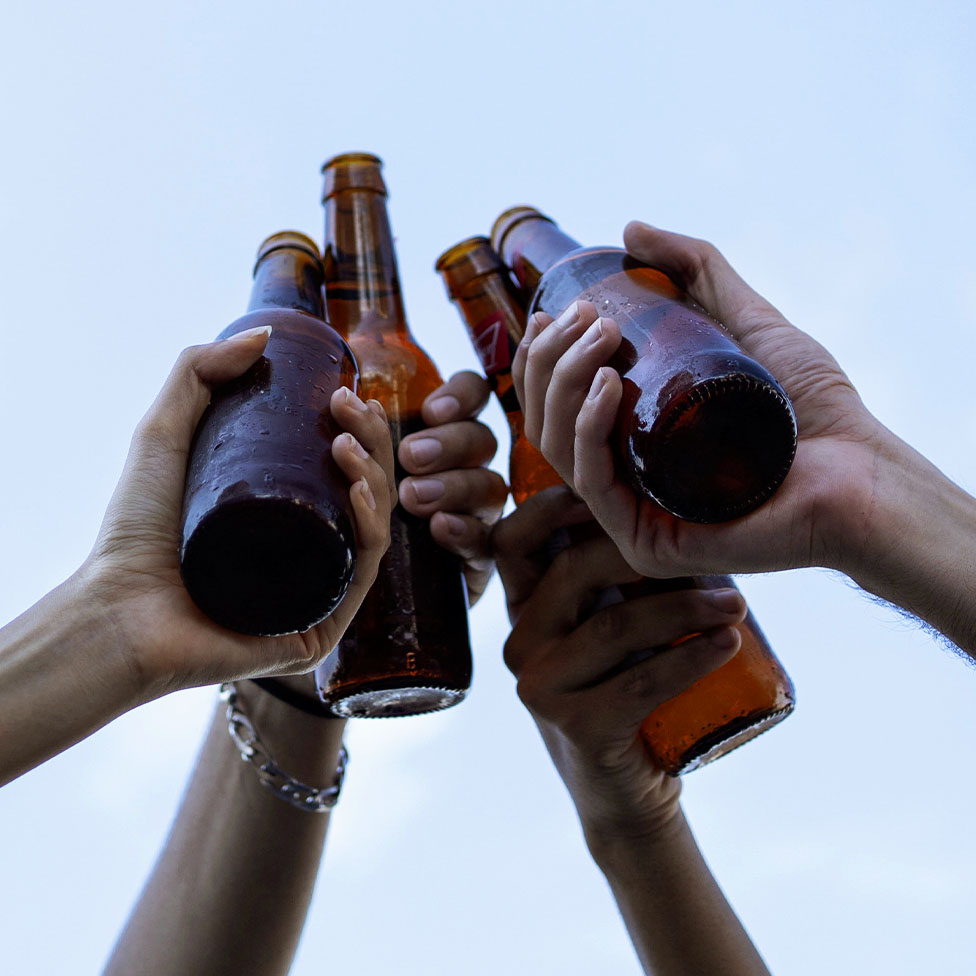 Four hands toasting with beer bottles in front of blue sky
