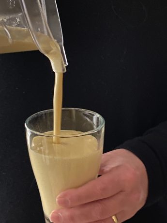 Mango lassi wordt ingeschonken in een glas vastgehouden door een hand