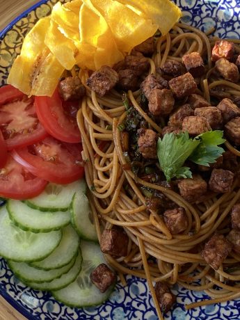 Een bord met Surinaamse bami, komkommer, tomaat en bananenchips