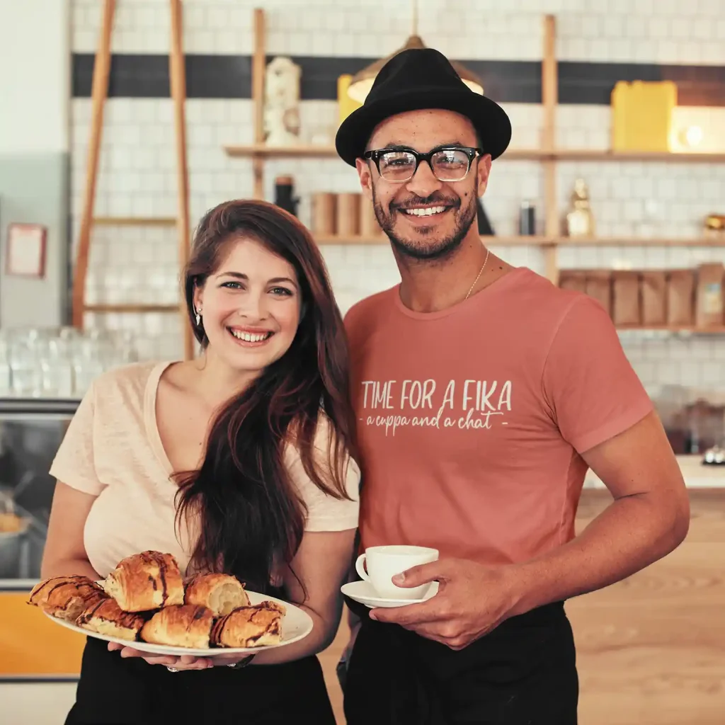 Couple serving fika in cafe wearing a terracotta t-shirt with fika print