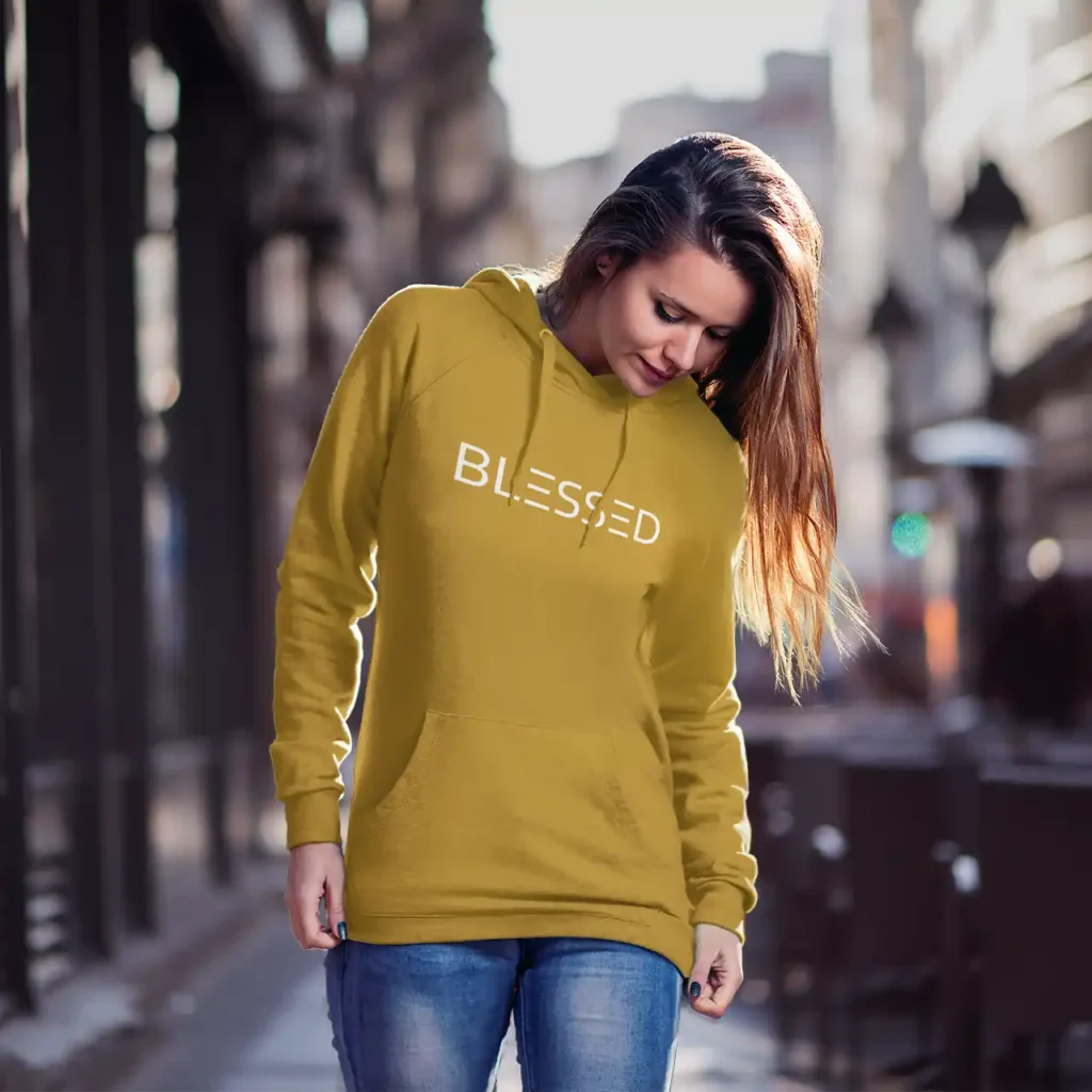 Young woman wearing mustard Just Hoods hoodie with white Blessed print