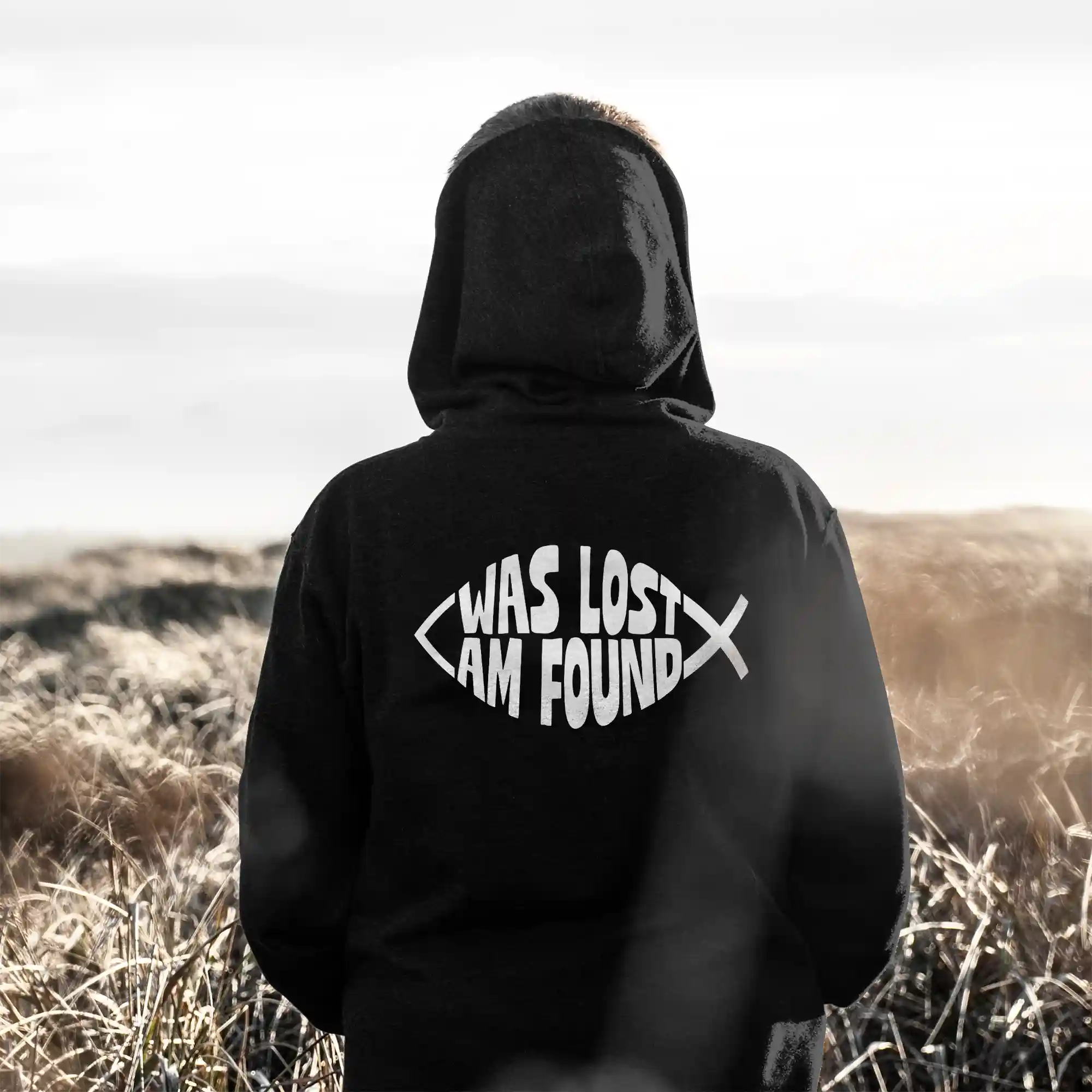 Person wearing a black Just Hoods hoodie with white Found print on the back