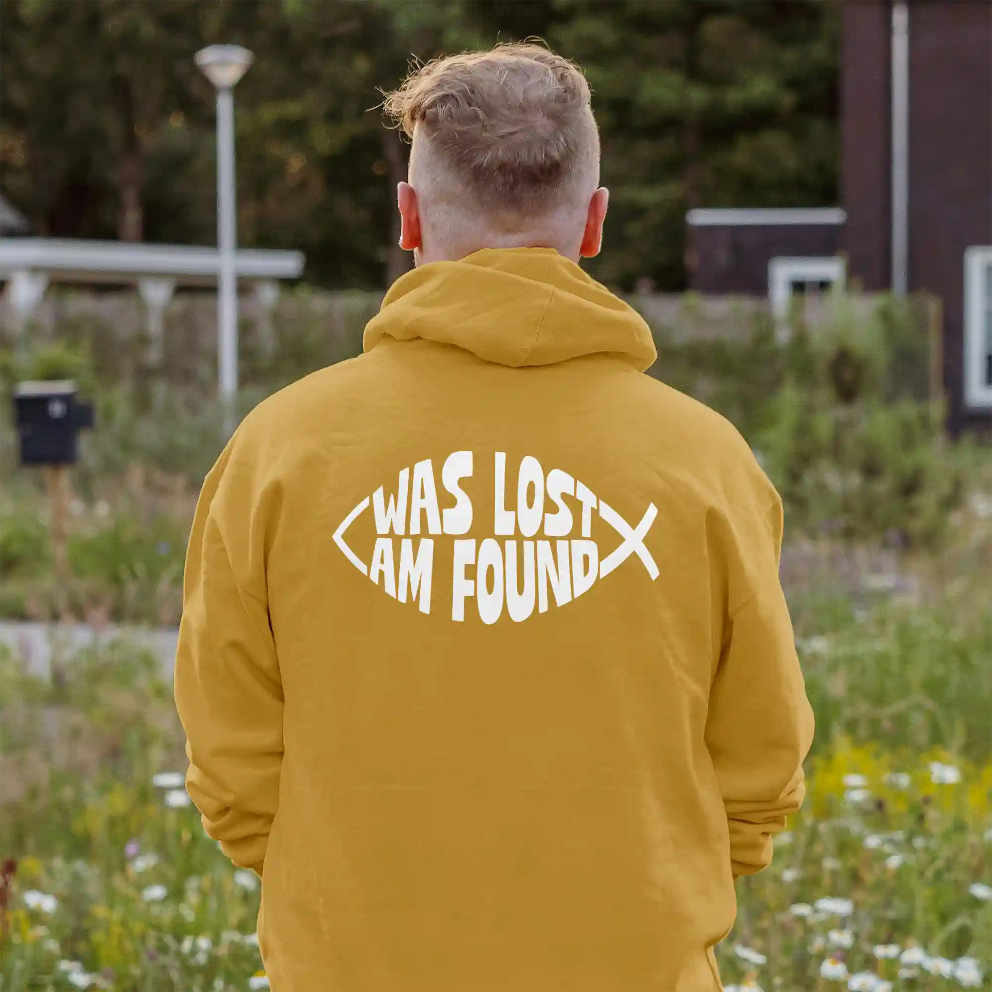 Man wearing a mustard Just Hoods hoodie with white Found print on the back