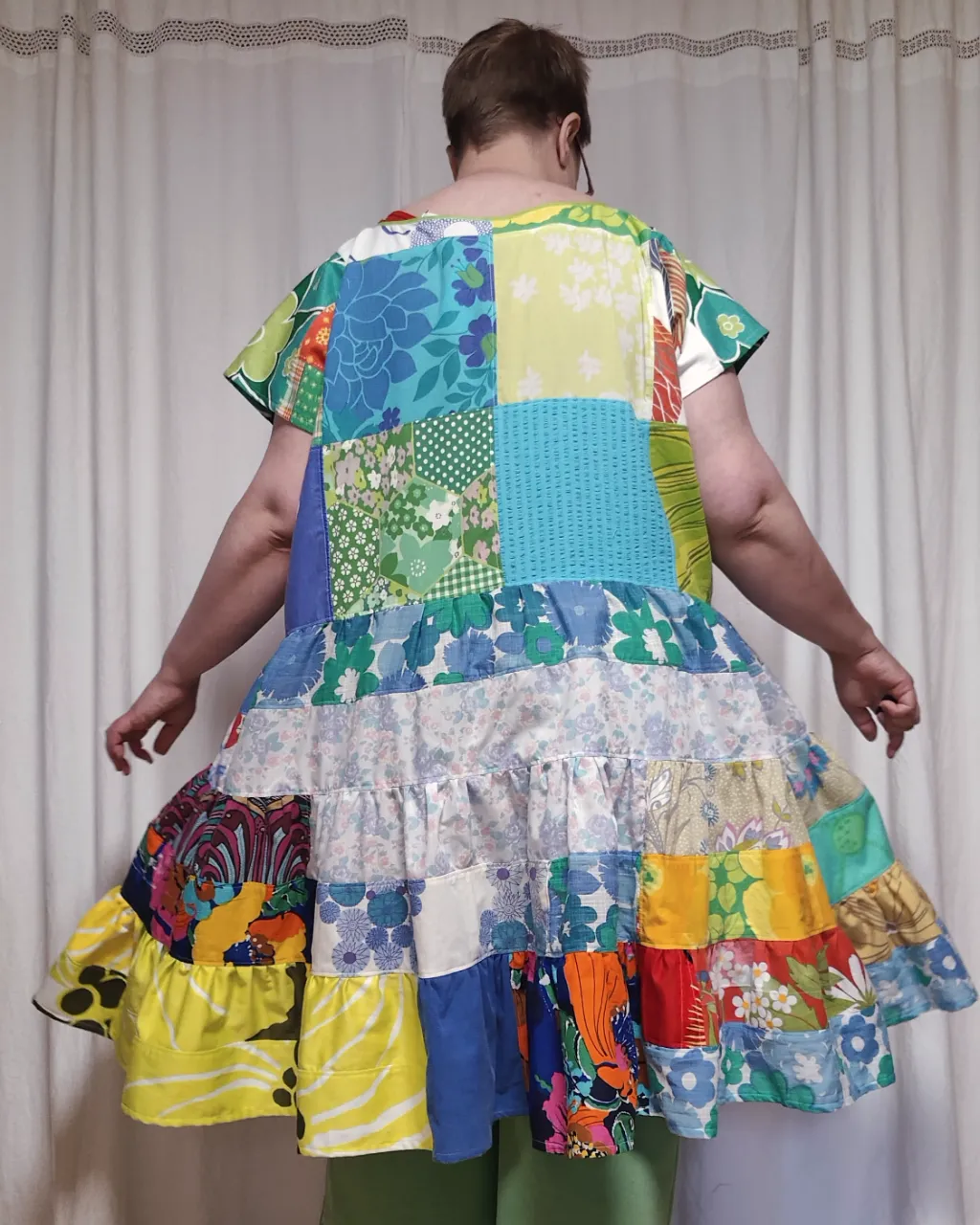 Medelålders tjock kvinna i en färgglad midiklänning i patchwork i gröna och blå färger sydd av slow fashion-företaget Skamlös Design