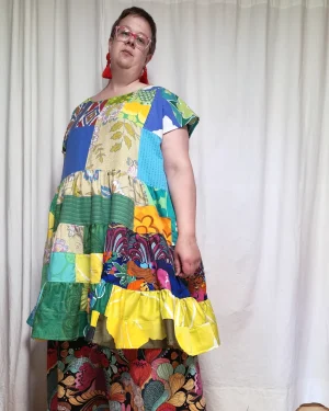 Medelålders tjock kvinna i en färgglad midiklänning i patchwork i gröna och blå färger sydd av slow fashion-företaget Skamlös Design