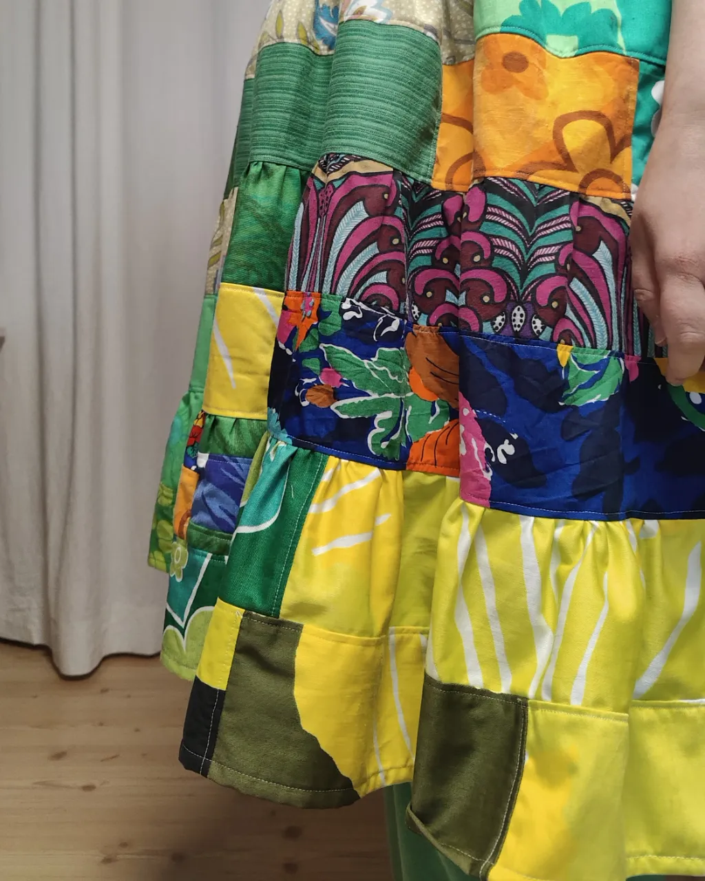 Medelålders tjock kvinna i en färgglad midiklänning i patchwork i gröna och blå färger sydd av slow fashion-företaget Skamlös Design