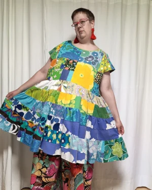 Medelålders tjock kvinna i en färgglad klänning i patchwork i gröna och blå nyanser sydd av slow fashion-företaget Skamlös Design